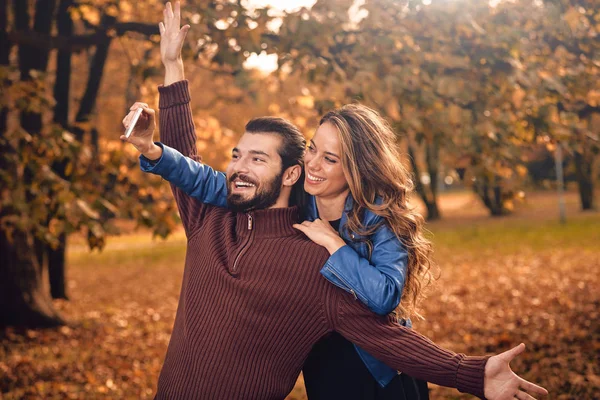 Junges Paar benutzt Handy im herbstlich gefärbten Park. — Stockfoto