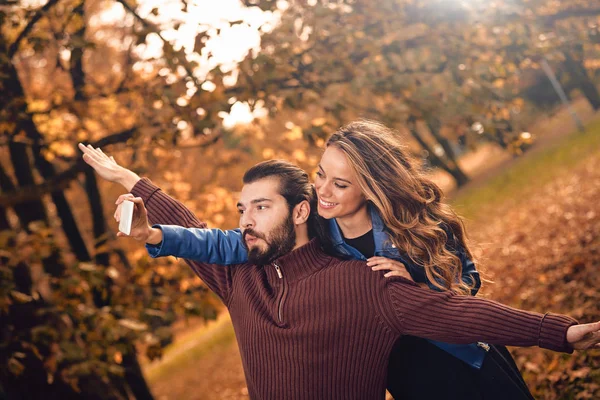 Junges Paar benutzt Handy im herbstlich gefärbten Park. — Stockfoto