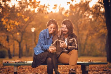 Genç çift sonbahar renkli park'cep telefonu kullanma.