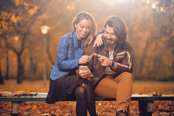 Giovane coppia utilizzando il cellulare in autunno colorato parco . — Foto Stock
