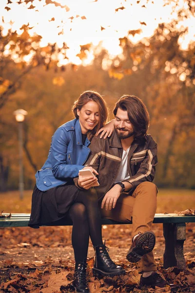 Junges Paar benutzt Handy im herbstlich gefärbten Park. — Stockfoto