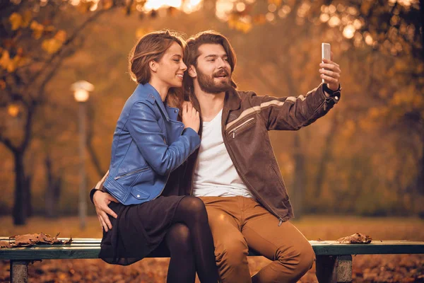 Молода пара використовує мобільний телефон в осінньому кольоровому парку . — стокове фото
