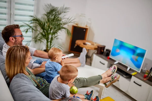 Padres jóvenes viendo televisión con niños pequeños . — Foto de Stock