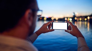 B 'de şehir ışıkları olan nehir kenarında cep telefonu kullanan bir iş adamı.