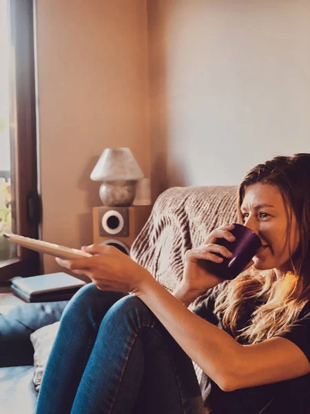 Mulher assistindo TV e bebendo café / chá em um sofá . — Fotografia de Stock