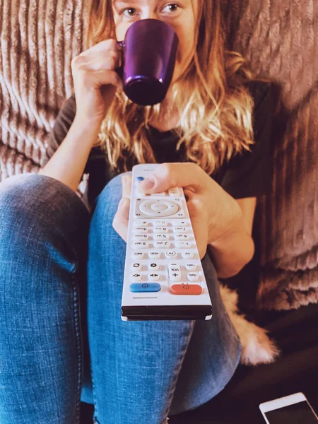 Mulher assistindo TV e bebendo café / chá em um sofá . — Fotografia de Stock