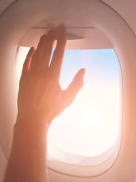 Passenger\'s hand closing the window shade on a modern airplane.