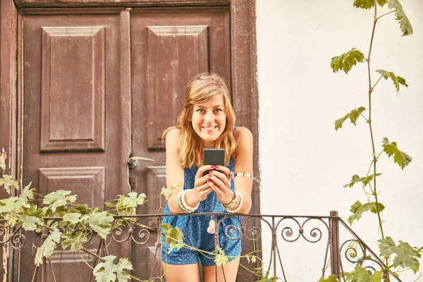 Jeune femme mignonne utilisant un téléphone portable sur le porche de la maison / terrasse . — Photo