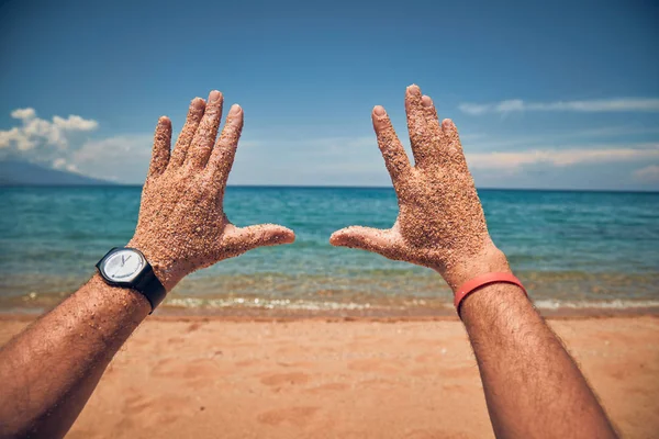 Man playing with his hands on a sandy tropical beach.