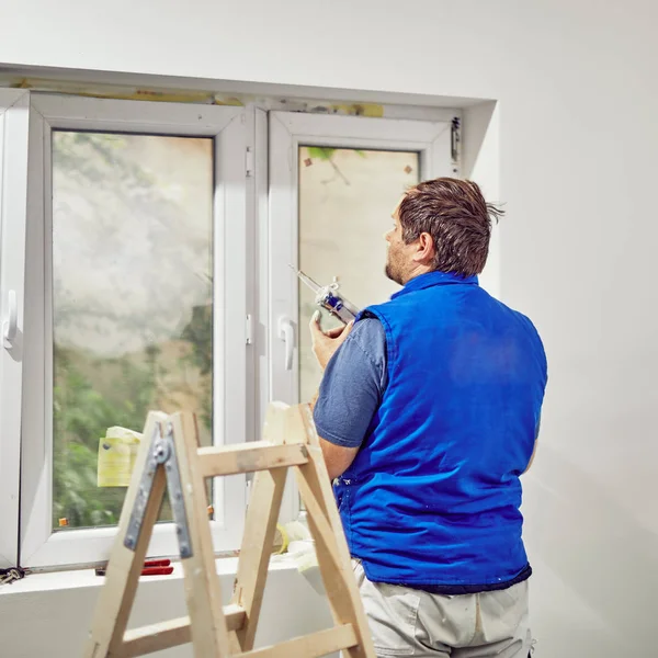 Worker using silicone for walls and widnows inside the house - r