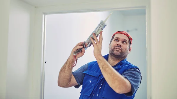 Trabajador que usa silicona para paredes y marco de puerta dentro de la casa — Foto de Stock