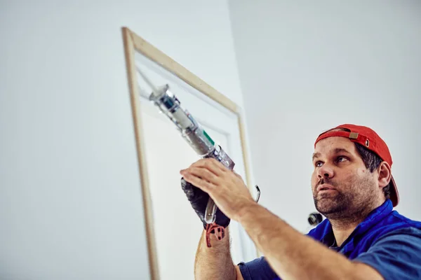 Trabajador que usa silicona para paredes y marco de puerta dentro de la casa — Foto de Stock