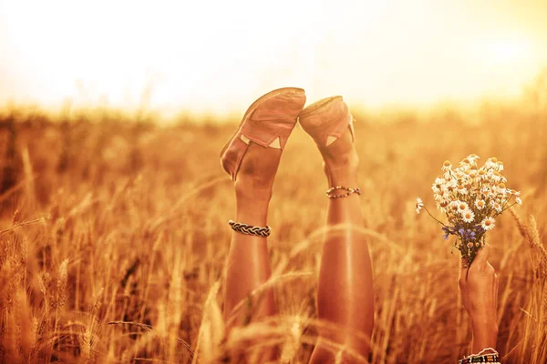 Girl holding flowers and lying in a wheat field. — Stock Photo, Image