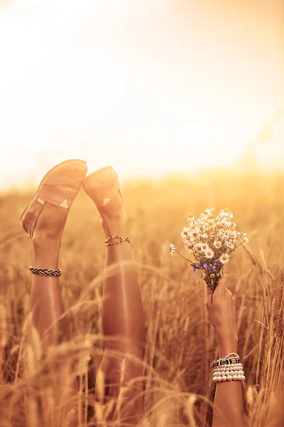 Ragazza che tiene fiori e giace in un campo di grano . — Foto Stock