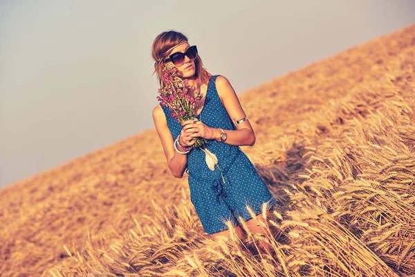 Woman with bouquet of flowers in a wheat field. — Stock Photo, Image