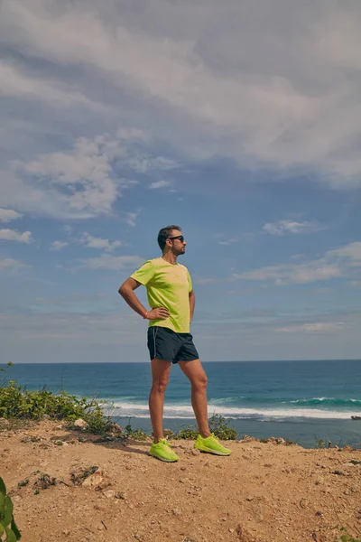 海の近くの熱帯のエキゾチックな崖の上に伸びるスポーツマン. — ストック写真