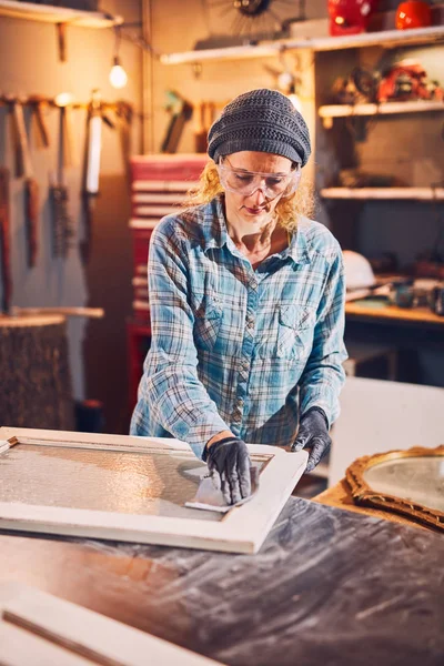 Carpintero mujer lijando ventana vieja en un taller retro . — Foto de Stock