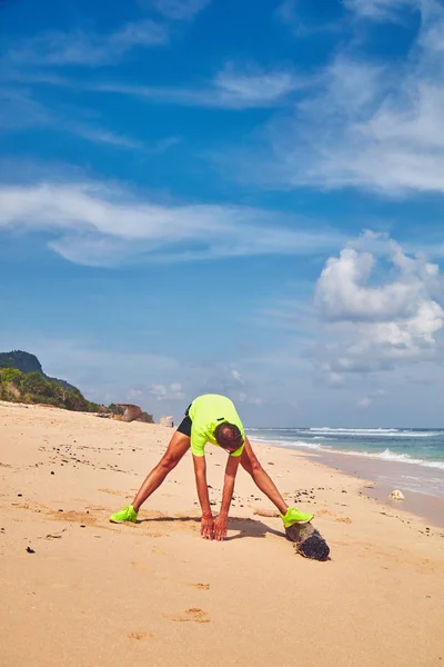 Sportsman stretching on a tropical sandy beach. — Stock Photo, Image