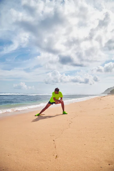 Sportman die zich uitstrekt over een tropisch zandstrand. — Stockfoto
