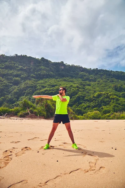 Esportista que se estende em uma praia tropical de areia . — Fotografia de Stock