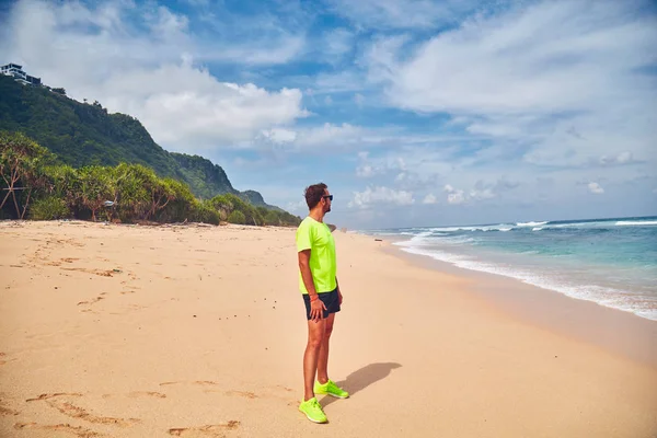 Sportman die zich uitstrekt over een tropisch zandstrand. — Stockfoto