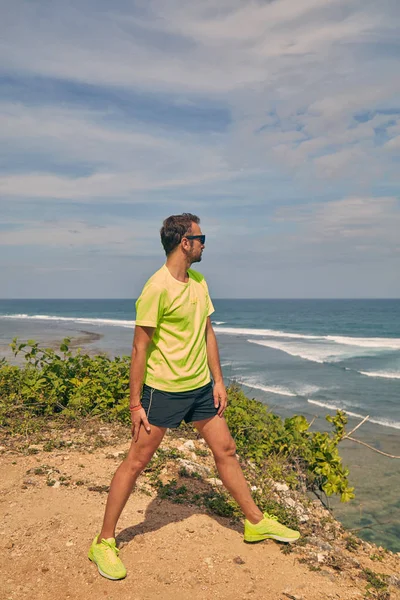 Deportista estirándose en un acantilado tropical exótico cerca del océano . —  Fotos de Stock
