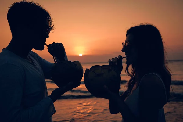 Pareja bebiendo jugo de coco mientras observa la puesta de sol sobre el océano en Bali, Indonesia . —  Fotos de Stock