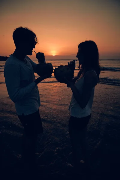 Casal beber suco de coco enquanto assiste o pôr do sol sobre o oceano em Bali, Indonésia . — Fotografia de Stock