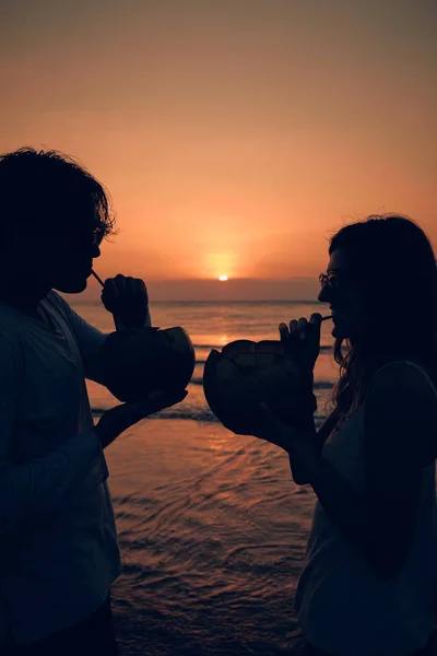 Pareja bebiendo jugo de coco mientras observa la puesta de sol sobre el océano en Bali, Indonesia . —  Fotos de Stock