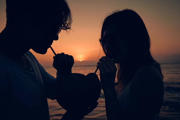 Pasangan tersebut meminum jus kelapa sambil menyaksikan matahari terbenam di atas lautan di Bali, Indonesia . — Stok Foto