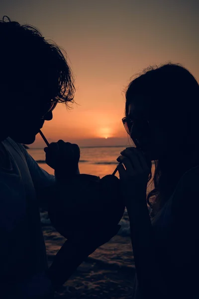 Casal beber suco de coco enquanto assiste o pôr do sol sobre o oceano em Bali, Indonésia . — Fotografia de Stock