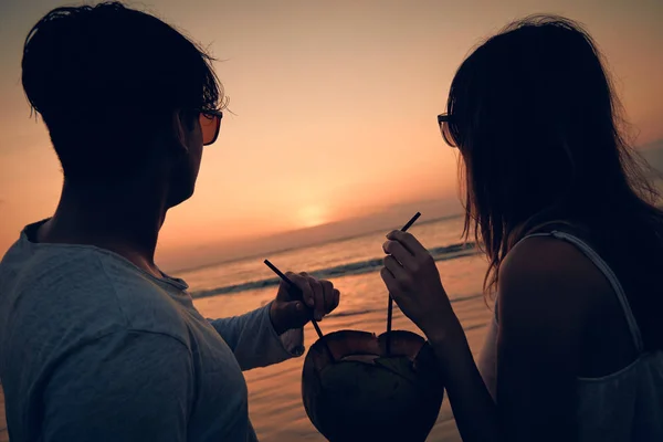 Pareja bebiendo jugo de coco mientras observa la puesta de sol sobre el océano en Bali, Indonesia . —  Fotos de Stock