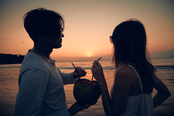 Pareja bebiendo jugo de coco mientras observa la puesta de sol sobre el océano en Bali, Indonesia . —  Fotos de Stock