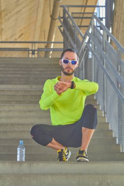 Büyük bir şehir köprüsünde kol saatine bakan sporcu.
