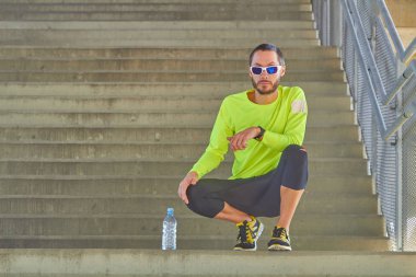 Büyük bir şehir köprüsünde kol saatine bakan sporcu.