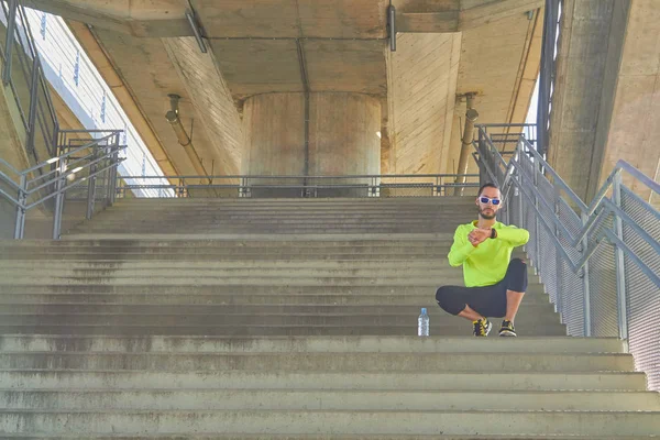Sportler blickt auf seine Armbanduhr auf einer großen städtischen Brücke. — Stockfoto