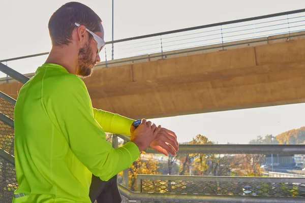 Deportista mirando su reloj de pulsera en un gran puente urbano . — Foto de Stock