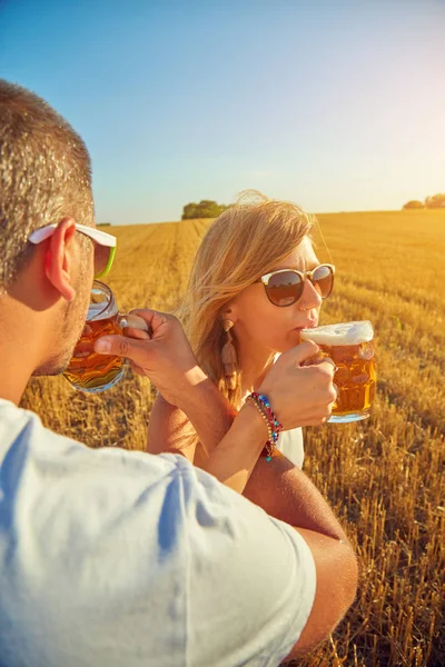 Молодая пара пьет пиво на открытом воздухе и наслаждается летом . — стоковое фото