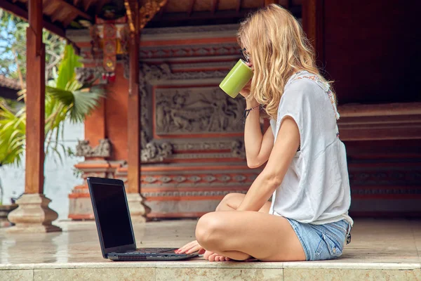 Chica freelancer con café / té y portátil en un porche casero . — Foto de Stock