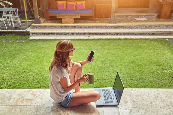 Chica freelancer con teléfono inteligente, café / té y portátil en una ho — Foto de Stock