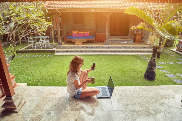 Chica freelancer con teléfono inteligente, café / té y portátil en una ho — Foto de Stock