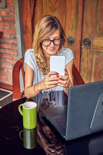 Chica freelancer con teléfono inteligente, café / té y portátil en una ho —  Fotos de Stock