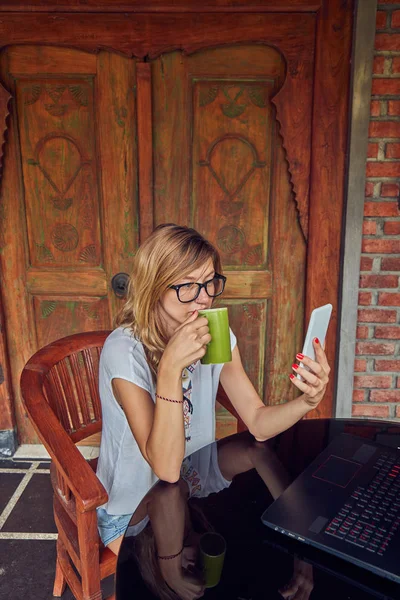 Ragazza freelance con smartphone, caffè / tè e laptop su un ho — Foto Stock