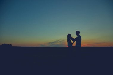 Gün batımı / gün doğumu saatinde bir çiftin siluetleri.