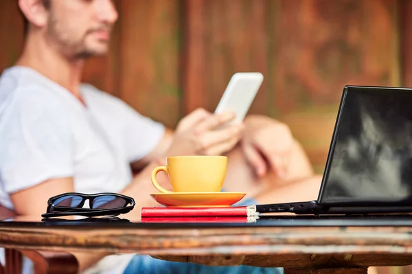 Muž s smartphone, kávou, čajem a notebookem na verandě. — Stock fotografie