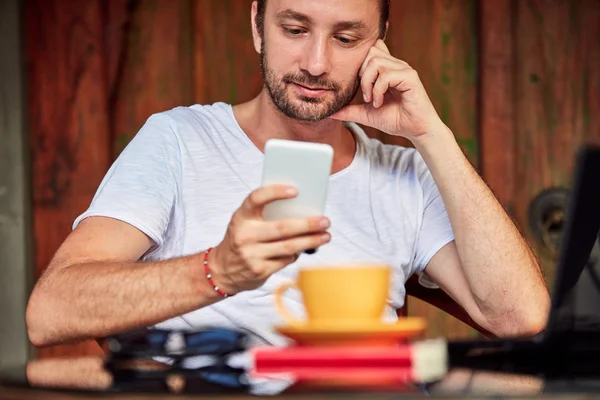 Hombre con teléfono inteligente, café / té y portátil en un porche de casa . — Foto de Stock