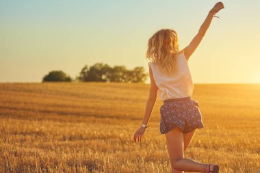 Sevimli genç kadın bir buğday tarlasında atlama.