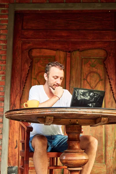 Hombre con teléfono inteligente, café / té y portátil en un porche de casa . — Foto de Stock