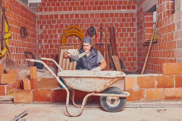 Настоящий строитель кладет кирпич на стену в помещении
.
