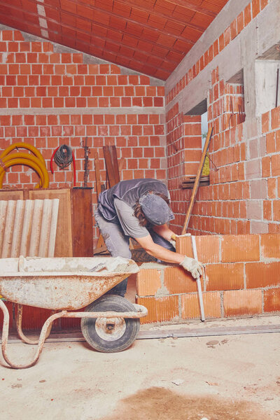 Настоящий строитель кладет кирпич на стену в помещении
.